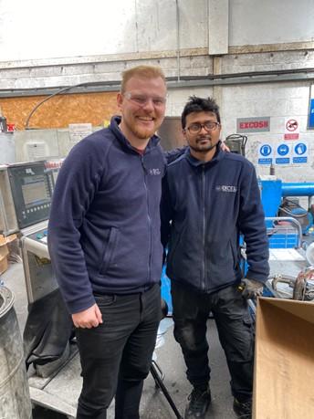 Two men stood smiling at the camera in a metal spinning workshop