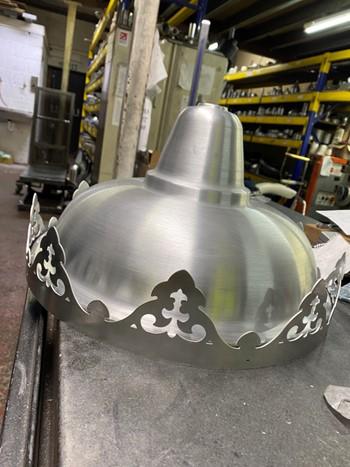 A metal light shade with detailed edges on a work surface in a workshop